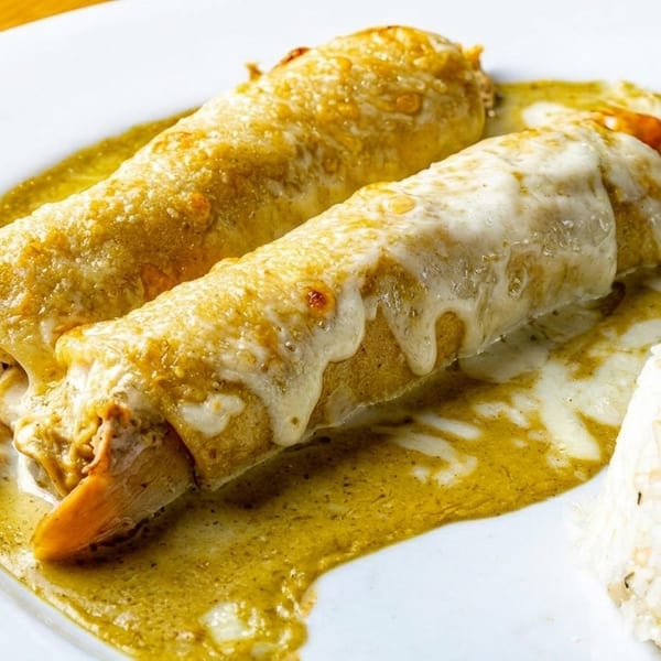 Two chicken enchiladas with green sauce and melted cheese, served with a side of white rice.