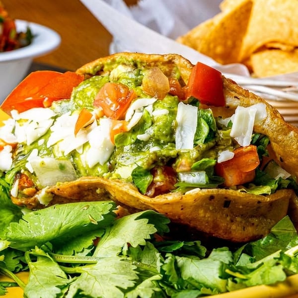 Crispy taco shell filled with guacamole, tomatoes, cheese, and cilantro, served with chips and salsa.