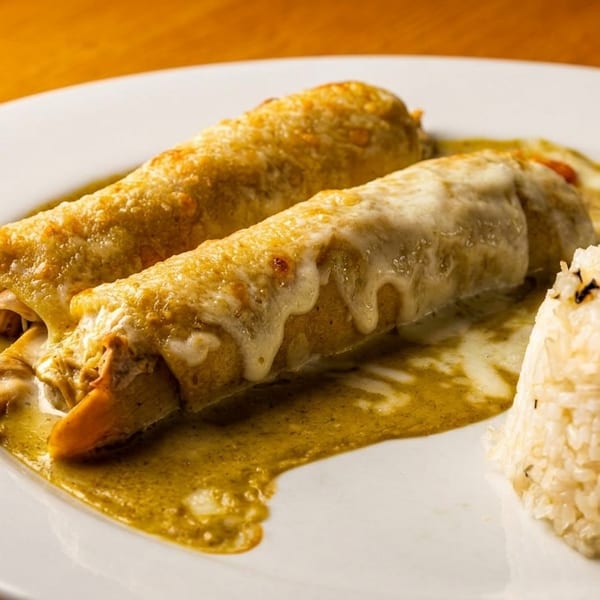 Two cheesy enchiladas covered in green sauce, served with a side of rice on a white plate.